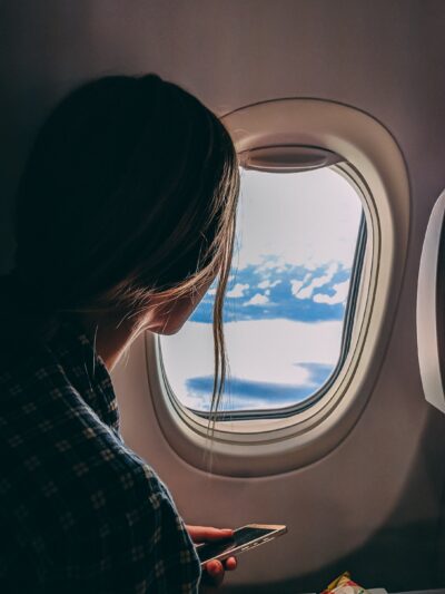 Meisje die uit het vliegtuig raam kijkt en op haar mobiele telefoon checkt 'vlucht compenseren'